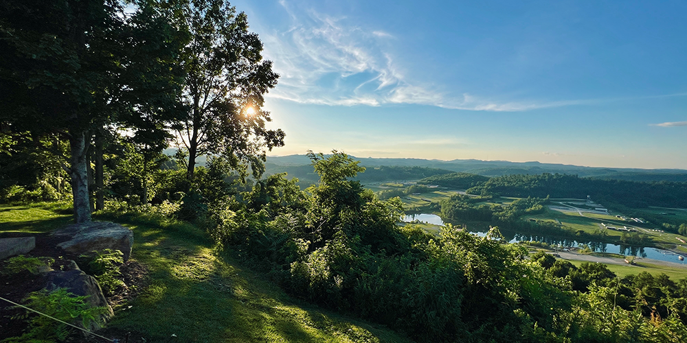 landscape image of appalachian mountains with sun shining through trees and a bright blue sky